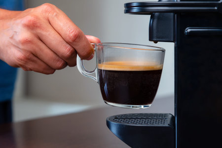 Close up of hand picking up a cup of espresso of capsule coffee machine at home. Concept of coffee...