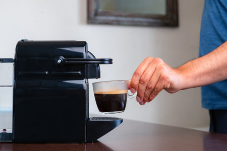 Close up of hand picking up a cup of espresso of capsule coffee machine at home. Concept of coffee break.の写真素材