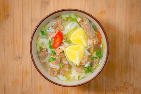 Spicy pho soup bowl with beef meat, lemon slice and chilli peppers on wooden table. Home delivery