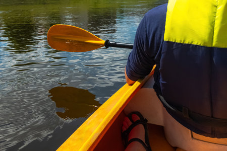 Close up shot of person canoeing in the river on a sunny day. Hands holding a paddle and rowing in...