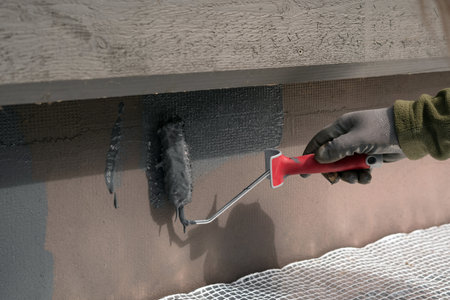 Man painting home socle with paint roller. Close up of rolling grey paint on building plinth. Home renovationの写真素材