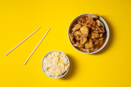 Crunchy fried sweet chicken plate with rice bowl and chopsticks on yellow background. Chinese food take away.の写真素材