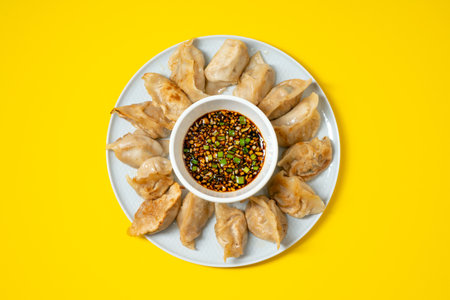 Fried gyoza style dumplings in a plate with spicy soy sauce on yellow background. Take away asian food.の写真素材