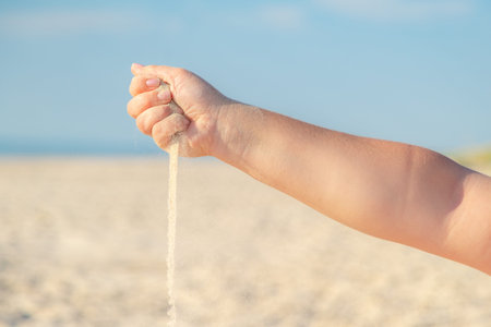 Close up of sand pouring from the hand on the beach on a sunny summer day. Playing with sand on vacation.の写真素材