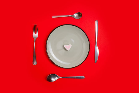 Romantic valentines day dinner idea concept. Heart on plate and silver wear on red background.の写真素材