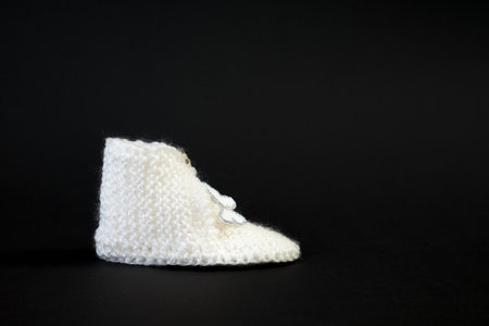 Handmade knitted white shoes for small children. Adorable newborn baby shoes isolated on black background.の写真素材