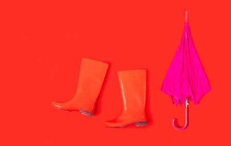 Rubber shoes and umbrella isolated on red background. Rain season and weather forecast. Nobodyの写真素材