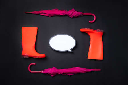 Rubber shoes, umbrella and speech bubble on black background. Rain season and weather forecast. Nobodyの写真素材