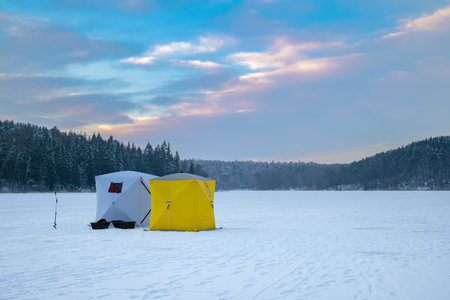 Ice fishing tent on a frozen lake at sunset. Fisherman camp on a peaceful winter evening.の写真素材