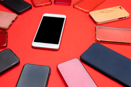 Choice of multicolored plastic back covers for mobile phones on red background with a smart phone on the sideの写真素材