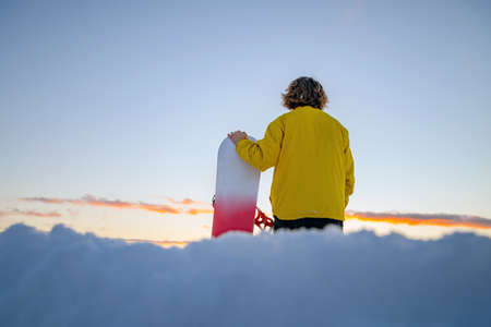 Snowboarder holding a snowboard on top of the mountain and looking reflecting into a distance. Winter holidays.の写真素材