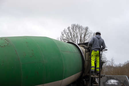Man worker on a ladder checking concrete mixer truck. Construction worker in housing development.の写真素材