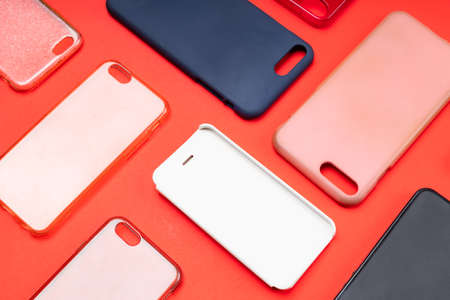 Pile of multicolored plastic back covers for mobile phone. Choice of smart phone protector accessories on red background. A lot of silicone phone backs or skins next to each otherの写真素材