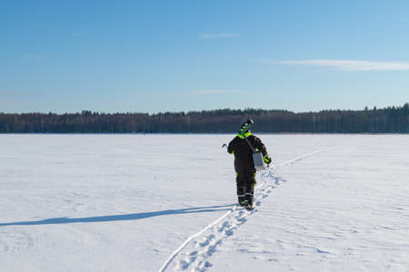 Man with fishing equipment walking on a frozen lake into the distance on a sunny winter day.の写真素材