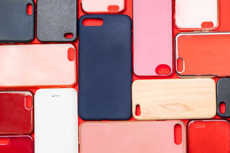 Pile of multicolored plastic back covers for mobile phone. Choice of smart phone protector accessories on red background. A lot of silicone phone backs or skins next to each otherの写真素材