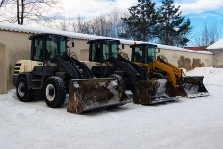 Heavy duty earth movers parked next to each other used to move snow after blizzard. Industrial excavators removing snow of the sidewalks.の写真素材