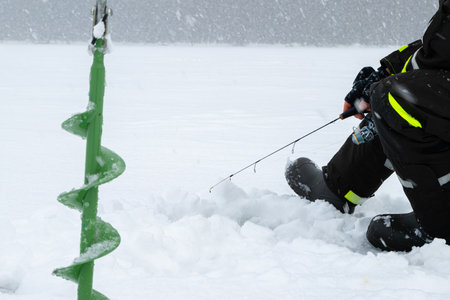 Winter fishing on ice. Man jiggling bait in an ice hole. Relaxing in the wild during snowfall.の写真素材
