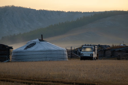 Nomadic yurt in the countryside with the mountains in the background on a sunny evening. Ger tent in the rural country surrounded by forest and hills, car parked next to it.の写真素材