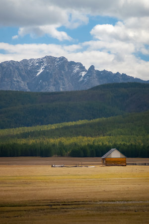 House in the countryside with the mountains in the background. Farm cabin in the rural country surrounded by forest and hills with the snowy tops.の写真素材