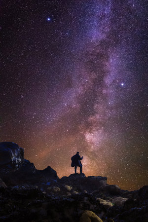 Silhouette of a man standing on a rocky mountain at night and looking at Milky Way. Inspiring view of stars in the sky.の写真素材
