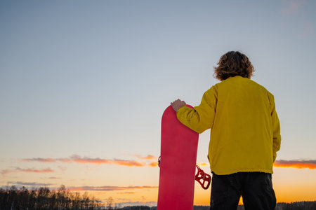 Snowboarder holding a snowboard on top of the mountain and looking reflecting into a distance. Winter holidays.の写真素材