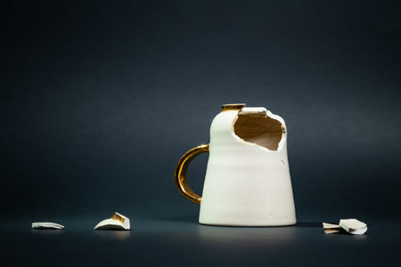 Broken tea cup isolated on black background. Cracked coffee mug and fragile ceramic pieces