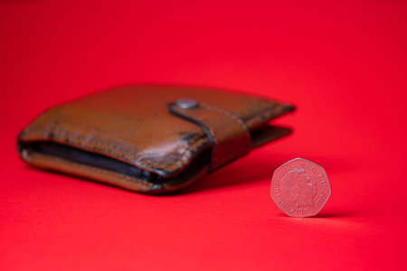 English money - fifty pence on red backdrop. Blurred wallet in the background. Saving money for...