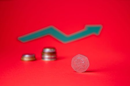 English money - fifty pence on red backdrop. Blurred growth sign in the background. Saving money for...