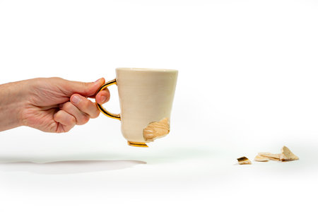 Man holding broken tea cup isolated on white background. Close up of arm holding cracked coffee mugの写真素材