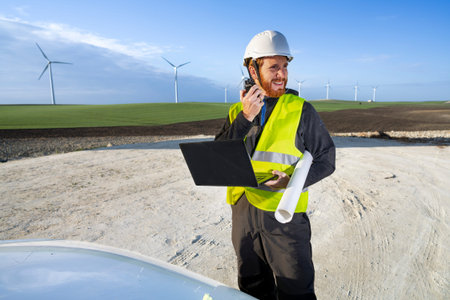 Engineer talking on the phone and looking at a laptop in a wind turbine park