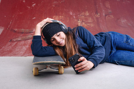 Teenager girl with skateboard listening to music on the street.