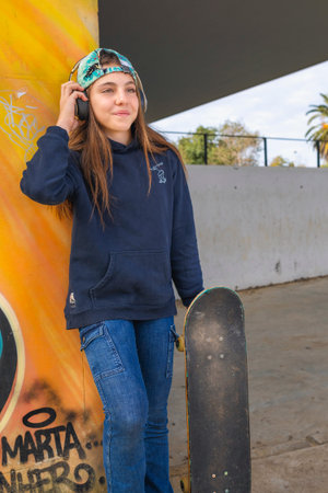 Young woman with skateboard listening to music on the phone in skate parkの写真素材