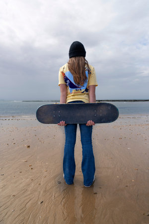 Rear view of a young woman with a skateboard on the beach