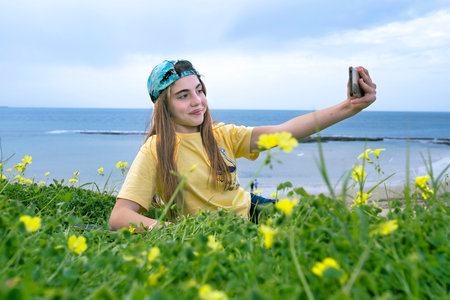 Teenage girl taking a selfie on the beach with yellow flowers.の写真素材