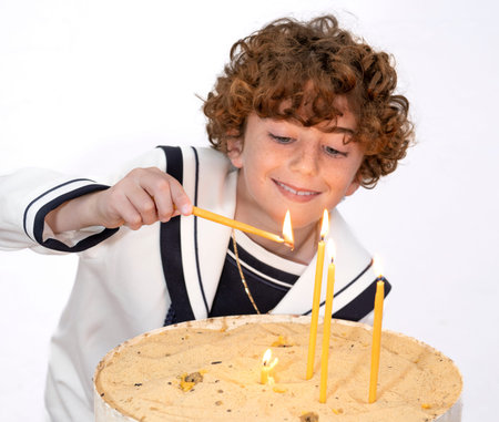 Boy lighting candles making la primera comunion on a birthday cake, isolated on white background.の写真素材