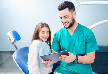 Cheerful dentist sharing tablet with patient on medical equipmentの写真素材