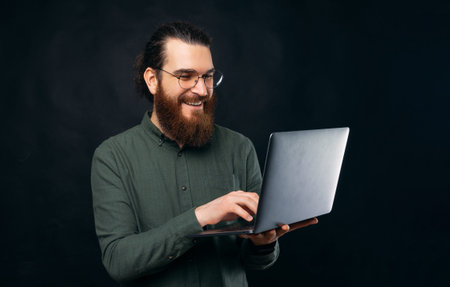 A bearded male is typing something in his laptop happily