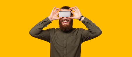 A bearded man holding a phone above his eyes .の写真素材