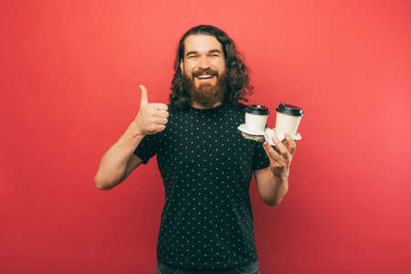 A photo of a bearded young man holdng some cups of coffeeの写真素材