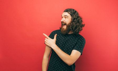 A happily young bearded man is pointing at some free space