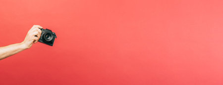 One man hand is holding a black camera over panorama coral background.