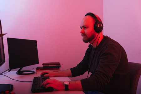 Bald bearded man wearing headset is sitting and working at the computer.
