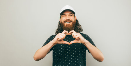 Portrait of cheerful young bearded man showing heart gesture with hands