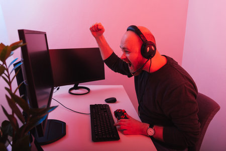 Young bald bearded man has won while playing games at the computer alone.
