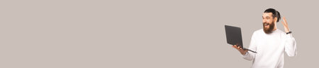Banner size photo of amazed young bearded hipster man looking at laptop over grey background