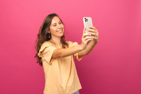 Photo of amezed young woman taking selfie with smartphone over pink backgroundの写真素材