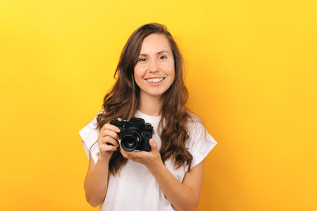 Close up portrait of young woman holding vintage photo camera over yellow background