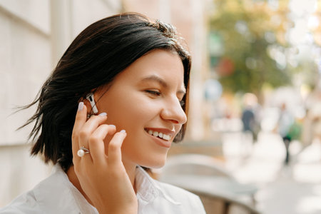 Close up portrait of young beautiful woman in casual using earpods near city background