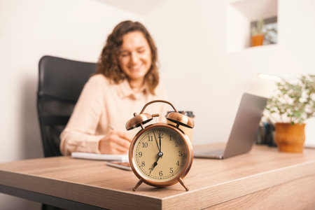 Close up photo of alarm clock on office table and woman making notes in agendaの写真素材