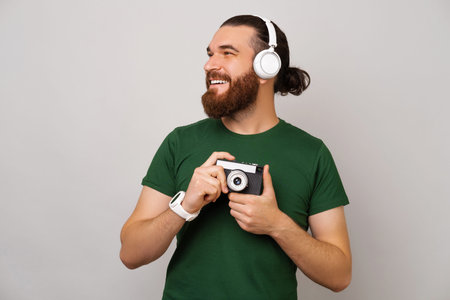 Phto of happy bearded hipster man in green t-shirt holdling old vintage camera and looking away over...